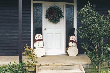 Log snowmen on doorstep in front of Christmas wreath.
