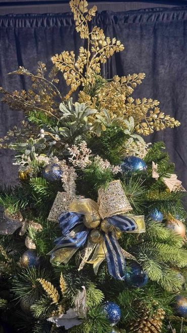 Closeup of Christmas tree topper with glitter gold leaves and mistletoe with blue decorations.