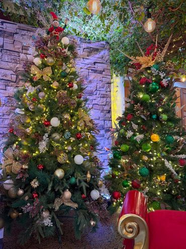 Friendly elf sitting on top of Snow-kissed Evergreen Christmas tree with additional red baubles.