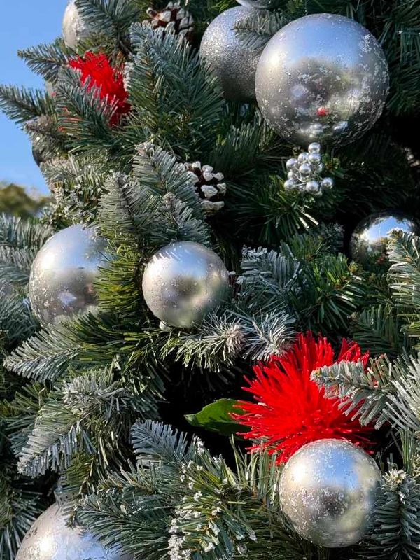 Closeup of mercury effect baubles, berry clusters and Pohutakawa flowers on flocked Christmas tree.
