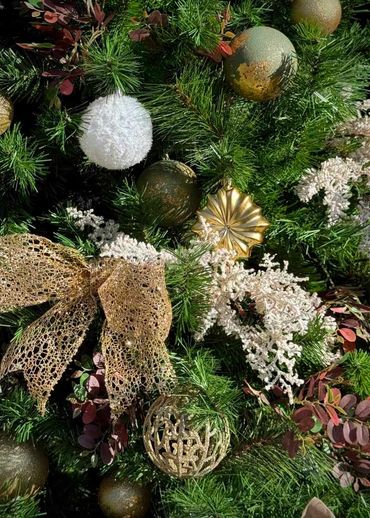 Closeup of sage green and gold Christmas tree decorations with snowy white bauble and foliage.