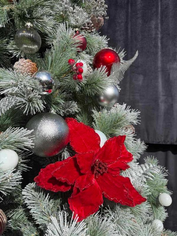 Closeup of Christmas tree decorations on snowy tree featuring red flowers and glass baubles.