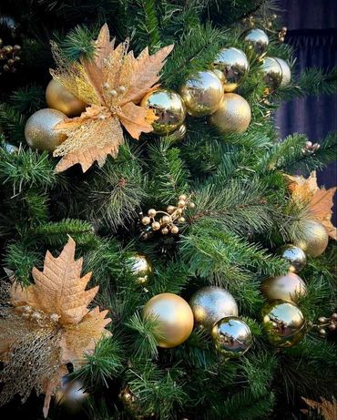 Closeup of gold poinsettia flowers, berries and bauble spiral on decorated Christmas tree.