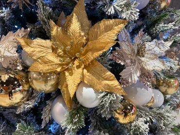 Closeup of white and gold bauble spiral and flowers on snowy look artificial Christmas tree.
