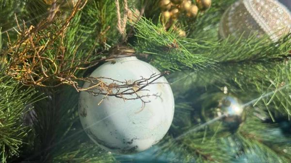 Closeup of porcelain bauble and gold twigs on artificial Christmas tree.