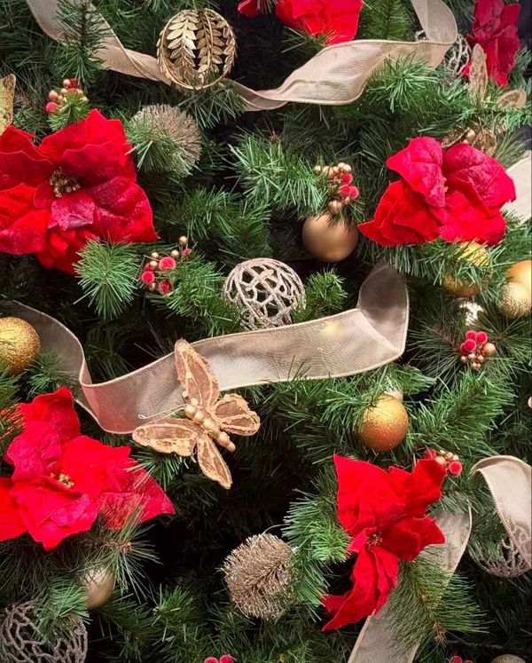 Closeup of gold and red Christmas tree decorations featuring berry clusters, ribbon and poinsettias.