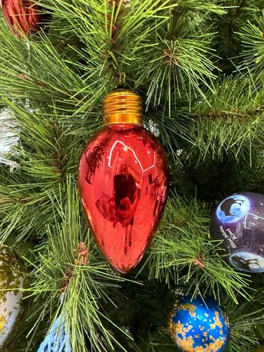 Closeup of red lightbulb Christmas decoration and kiwi bauble on realistic artificial pine tree.