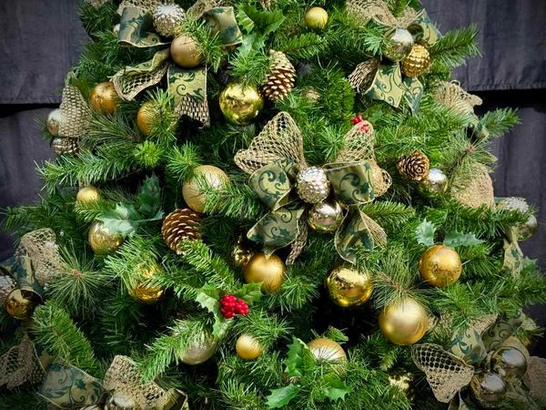 Closeup of our handmade green and gold bows with bauble centre, holly and pinecones plus baubles.