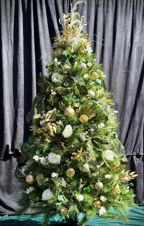 Luxury Christmas tree fully decorated with green and gold ribbon and decorations plus white roses.