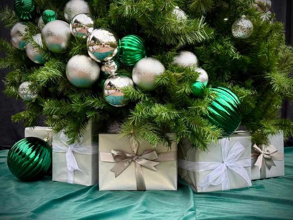 Fancy white and silver Christmas present stack with XL green baubles around base of Christmas tree.