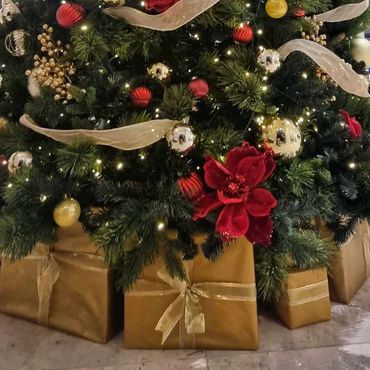 Closeup of Christmas decorations at base of tree featuring red & gold decorations & presents.