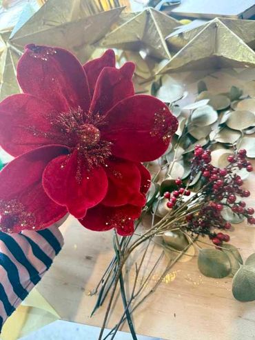 Closeup of velvet Christmas magnolia flower decoration with berries, & leaves on bench.