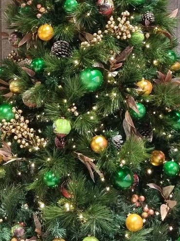Closeup of Christmas tree decorations and lights featuring snowy pinecones + gold and green baubles.