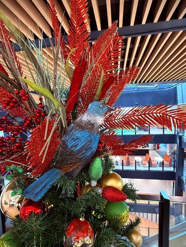 Closeup of handmade tub bird sitting on top of Christmas tree featuring glitter feathers & grasses.