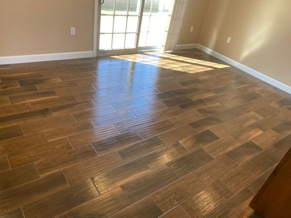 Sunlight reflects on polished wooden floor tiles in an empty room.