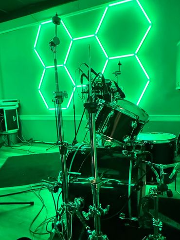 Drum set on stage with green hexagonal neon lights in the background.