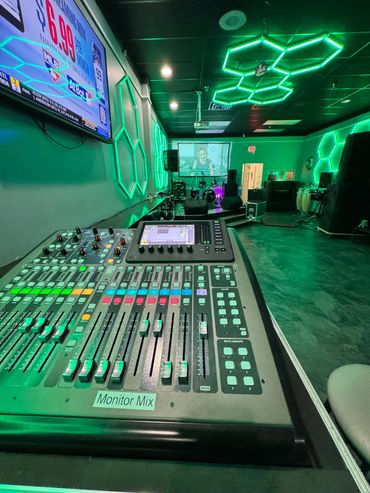 Sound mixing console in a vibrant green-lit music venue with stage and instruments.