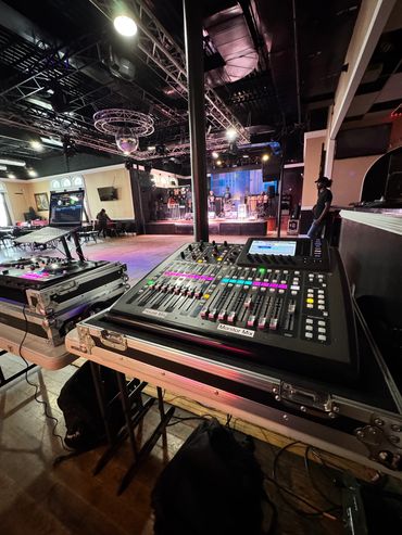 Sound mixing equipment set up in a music venue with a band on stage.