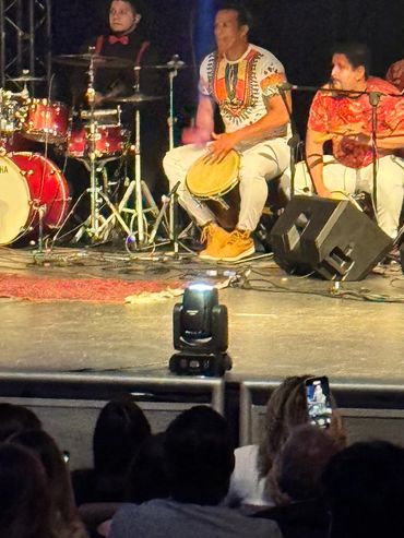 A lively musical performance with percussionists and a singer on stage in front of an audience.
