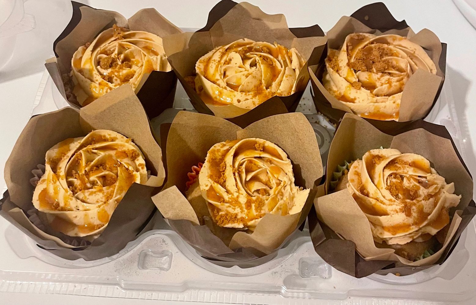 Six caramel-topped cupcakes with creamy frosting in brown parchment paper.