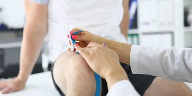 Therapist applying kinesiology tape on a patient's knee in a clinical setting.