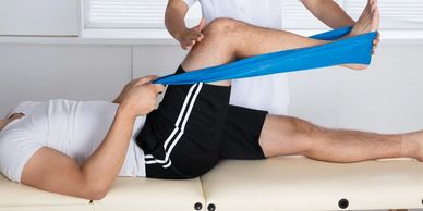 Physiotherapist assisting a man with leg resistance band exercises on a treatment table.