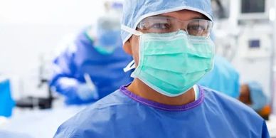 Medical professional in surgical attire wearing mask and protective eyewear.