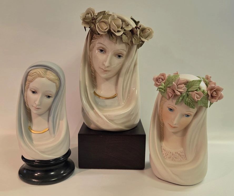 Three delicate ceramic busts of women with head coverings and floral crowns.