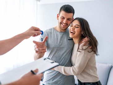 A happy young couple receiving keys from a person with a clipboard, symbolizing the successful