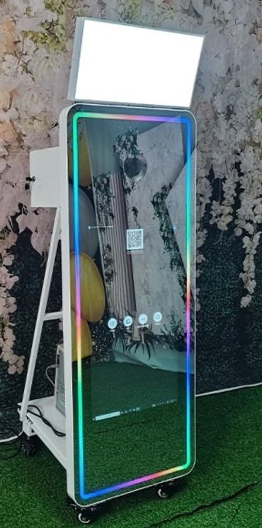 Tall photo booth mirror with colorful LED lights and a white softbox light above it.
