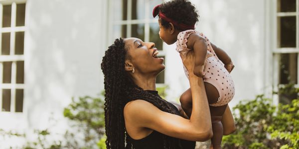 Mother joyfully lifting her baby outdoors in a sunny garden.