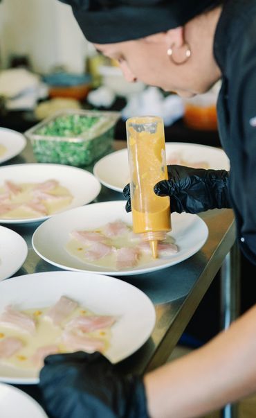Chef in black adding sauce to plates with fish.