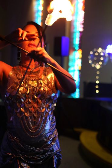 Performer in shiny outfit playing with fire in a dark room.