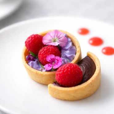Elegant raspberry and flower tart dessert with chocolate and purple cream.