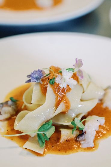 Gourmet pasta with creamy sauce, seafood, and edible flowers.