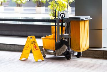Yellow cleaning cart with caution wet floor sign in a bright hallway.