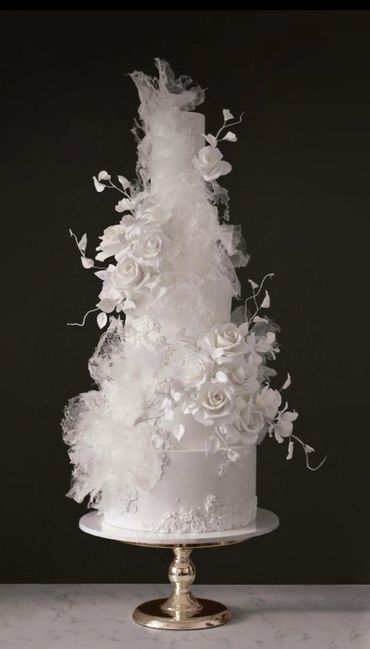 Elegant tall white wedding cake adorned with delicate sugar flowers and lace-like decorations.