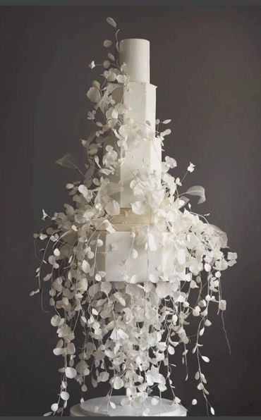 Elegant tall white wedding cake adorned with cascading delicate white floral decorations.