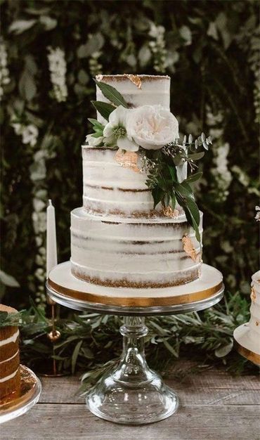 Elegant three-tier semi-naked cake decorated with white flowers and greenery.