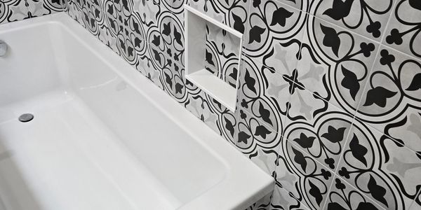 White bathtub with black and white patterned tiles on the wall.