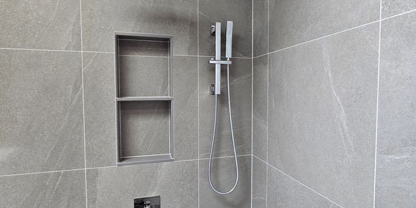 Modern gray tiled shower with built-in niche and handheld showerhead.