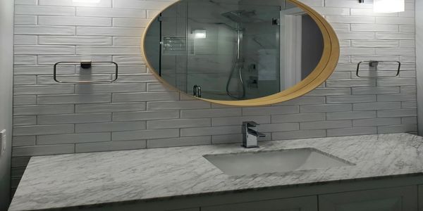 Modern bathroom with marble countertop and oval mirror.