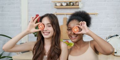 Two women holding tomato slices over their eyes, smiling.