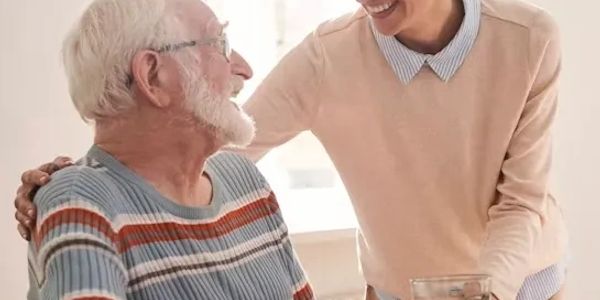 Caregiver comforting an elderly man with a warm smile.