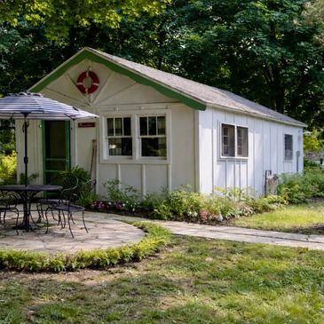 A charming white garden shed with green trim and outdoor seating.