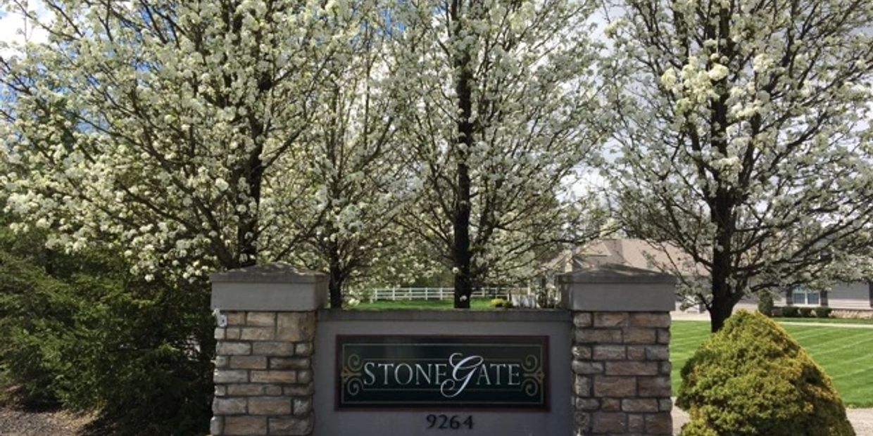 Entrance sign of Stone Gate community surrounded by blooming trees.