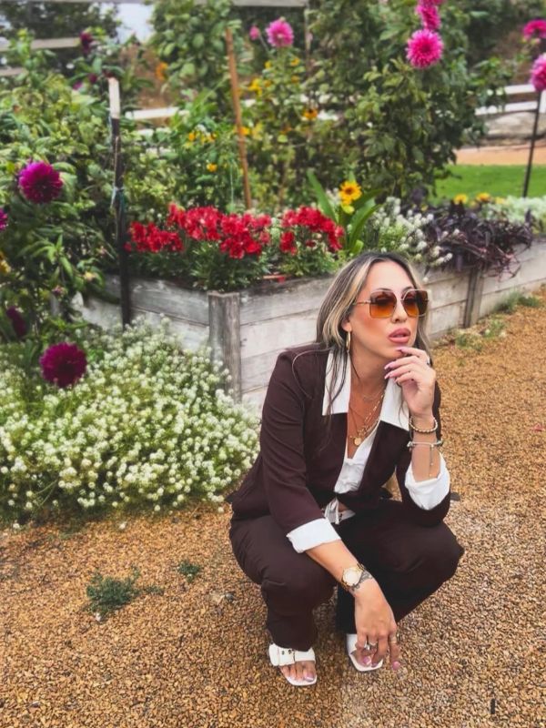 Woman in sunglasses crouching in a flower garden.