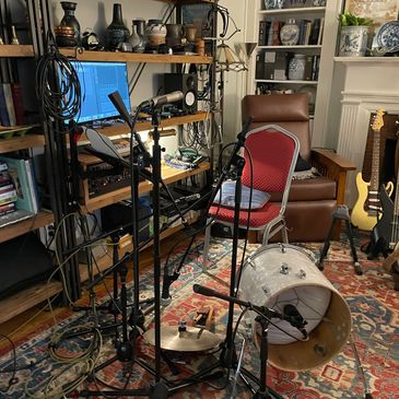 Home recording setup with microphones, drums, guitar, and computer.