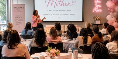 Woman leading a workshop with attentive attendees in a decorated room.