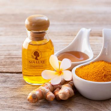 Natural skincare ingredients including turmeric powder, oil, and a flower on wood.
